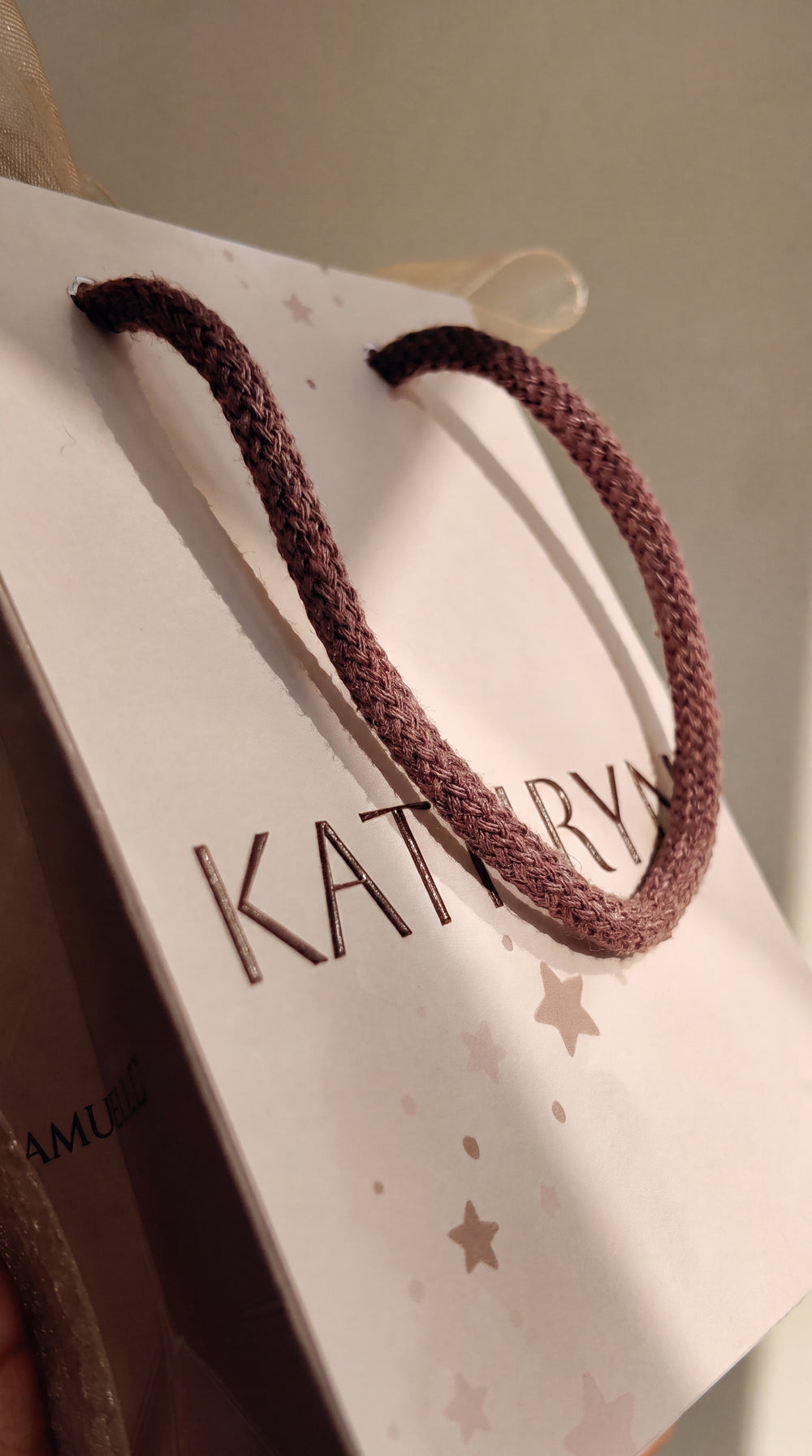 Personalised baby shower gift bag in soft brown with raised lettering, woven rope handle and sheer ribbon bow, styled on a neutral table