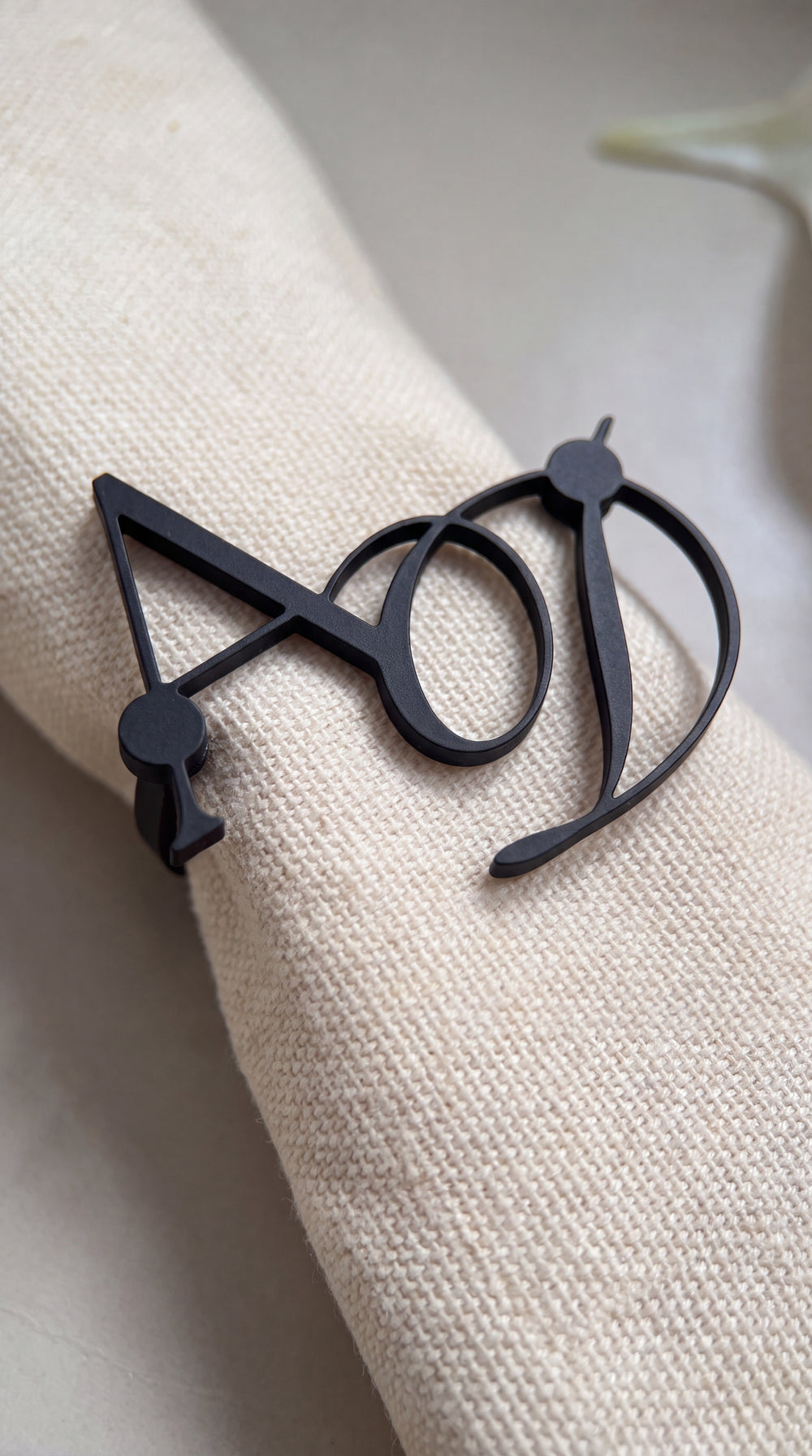Close up of a matte black entwined monogram napkin ring showing the magnetic close