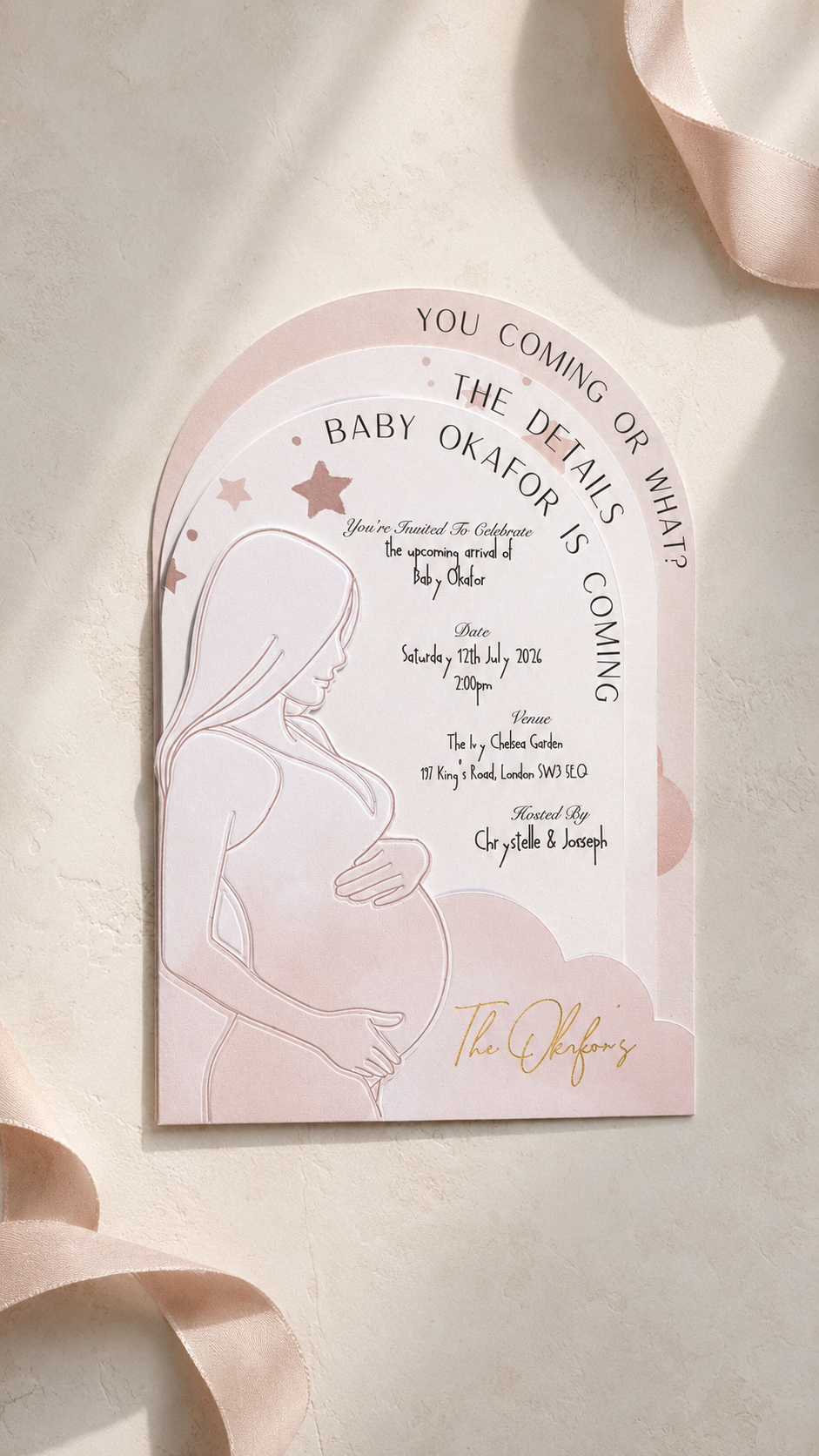 A pink and white arch-shaped baby shower invitation card featuring a pregnant woman silhouette, elegant script text, and gold foil accents, styled on a textured beige surface with soft pink ribbons.